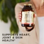 A woman holds up Solgar's Omega-3 Fish Oil Concentrate Softgels in an amber glass bottle. Text reads 'supports heart, joint, and skin health"